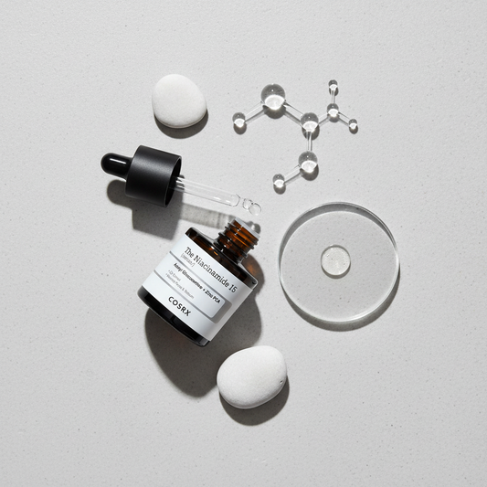 COSRX Niacinamide 15% + Zinc 1% Serum lifestyle flat lay on grey surface with white pebbles